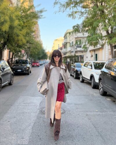 Stivali marroni arricciati abbinati a gonna rossa in velluto e pizzo e cappotto grigio oversize per un outfit autunnale da sera